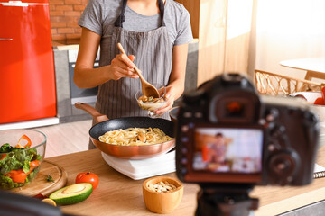Young woman adding mussels into pasta while recording cooking video class in kitchen