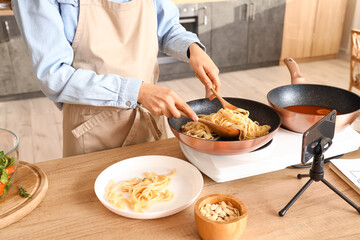 Young woman putting pasta onto plate while recording video class in kitchen, closeup
