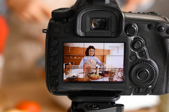 Young woman cooking pasta on display of photo camera in kitchen, closeup
