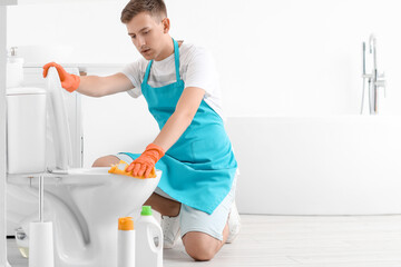 Young man cleaning toilet bowl with rag in bathroom