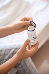 Young man with bottle of magnesium pills in bedroom, closeup
