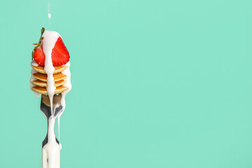 Fork with mini pancakes, fresh strawberry and pouring sauce on green background