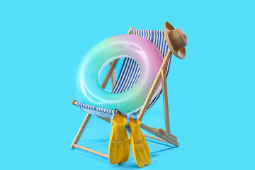 Wooden deck chair with inflatable ring, hat and paddles on blue background