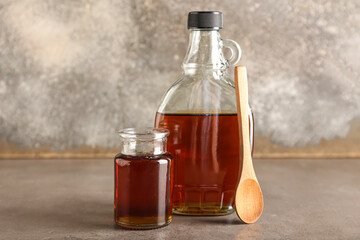 Bottles of maple syrup and spoon on grunge background