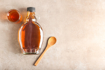 Bottle and glass of maple syrup on light background