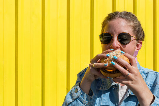 woman with sunglasses taking a bite of a big burger 