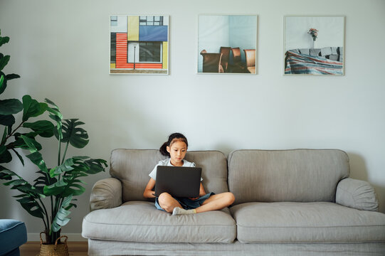 School girl e-learning on laptop in living room
