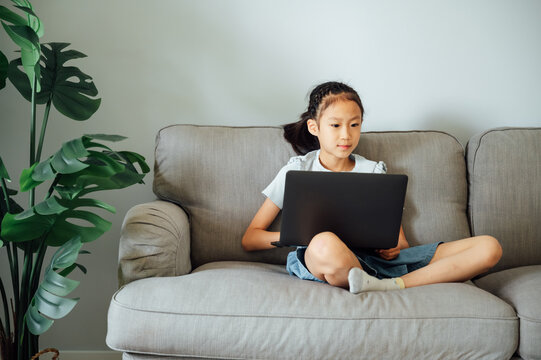 School girl e-learning on laptop in living room
