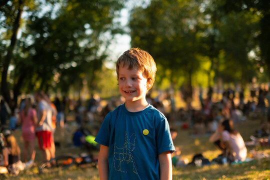 A blonde boy looks away from the camera in the park during the summer
