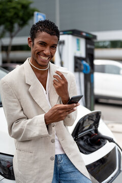 Black man using Smartphone While Recharging Electric Vehicle