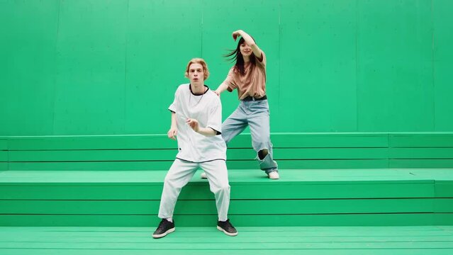 Young couple dancing hip hop on green background wall. Modern dance choreography. Professional dancers man and woman duet showing dance movings. Musical video.
