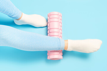 Female leg rolls a massage foam roller close-up on a blue background, top view.