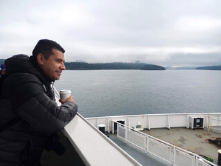 Latino adult man travels by boat watching the cold sea, rests from his job in Canada and lives the...