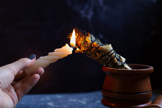 Herbal wand stick above burning candle isolated on black