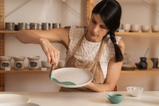 Female Potter Applying Glaze With A Brush On The Plate 