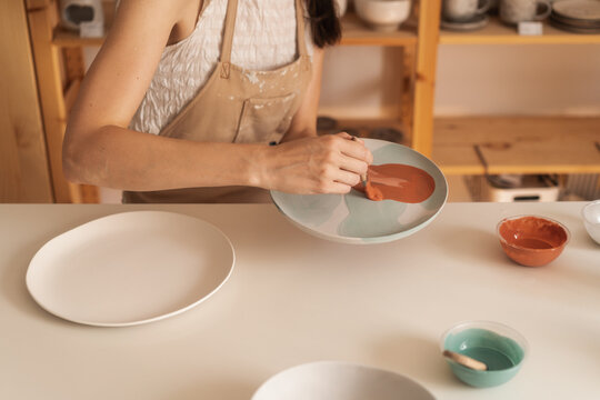 Anonymous Woman Applying Glaze On The Plate In The Pottery Workshop