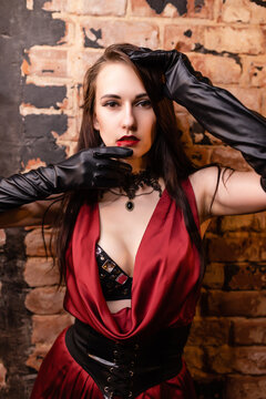 Beautiful girl in a red dress posing. Vampire image. Keeps hands close to face. Halloween concept, nightclub, masquerade