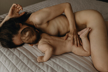 The newborn naked baby is lying on the bed near it's mother at home
