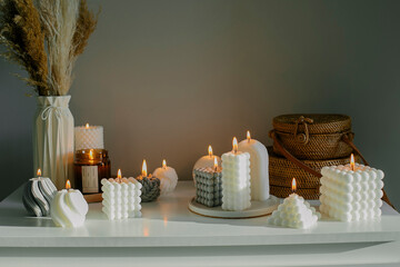 Home interior decor. White dresser with dried flowers in vase, rattan bags and variety candles. Still life, hygge concept