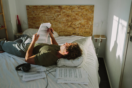 Man on a bed reading music sheet