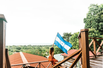 Female tourist waving the flag of Honduras in front of some mountain cabins.