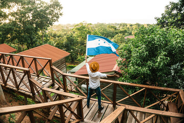 male tourist waving the flag of Honduras in front of some mountain cabins - obrazy, fototapety, plakaty