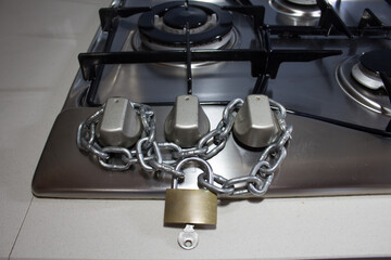Obraz premium Image of a chain with lock to close the knobs of a gas stove hob in a kitchen. Reference to the blockade, shortage and constant increase in the price of natural gas. 
