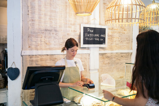 Worker of a pastry shop charging a client with the dataphone