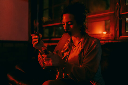 Woman in red light smoking a bong at home