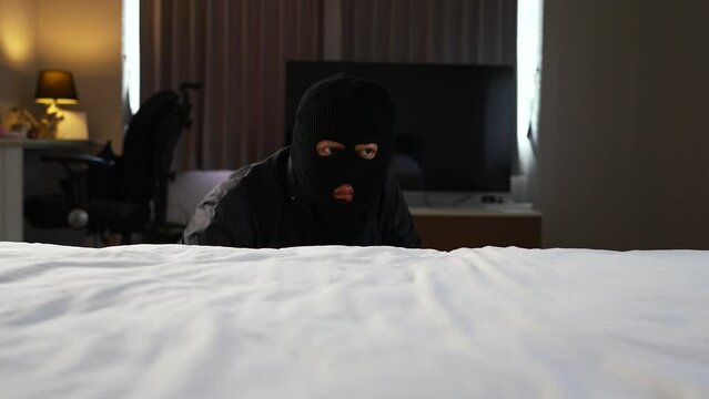 Burglar climbing up on the bed trying to search for valuables things in sleeping room.