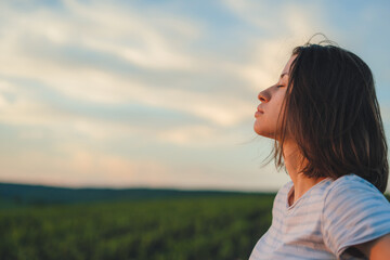 Profile view calm woman breathing fresh air and dreaming with eyes closed, standing int the cornfield. Wellbeing concept. Summer vacation. Harmony concept