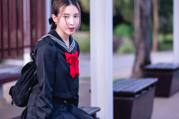 Woman wearing cosplay Japanese school uniform sitting at bus stop.
