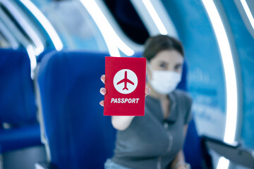 Woman wearing protective face mask sitting inside airplane and showing passport.