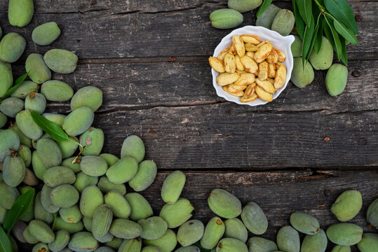 Green almonds open background   fresh raw unripe wooden rustic table blurred garden background leaves, Top view copy space shell  tree branch frame Peeled almond kernel milk husks white Bowl