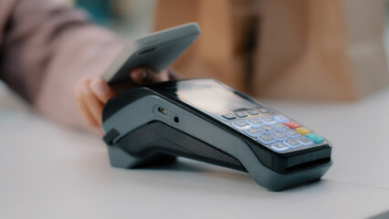 Woman at check-in desk at counter pays with smartphone through NFC contactless payment from mobile...