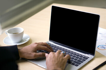 Back view of businessman in suit sit at desk in office typing on laptop computer keyboard with black screen.