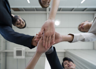 Team building concept. Coworkers standing in circle join hands together, celebrating business success in modern office with high ceiling. Bottom View