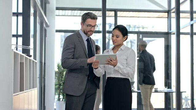 Businesspeople browsing on a digital tablet while discussing, planning and brainstorming together at work. Ceo or boss and young female intern talking after a meeting in a corporate startup office