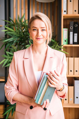 Blonde business lady in the office in a business suit with books in her hands