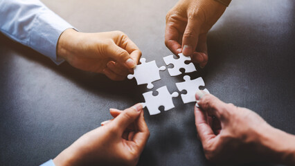 Close up four hands holding pieces of white jigsaw puzzle, joint path to problem solution, find way...