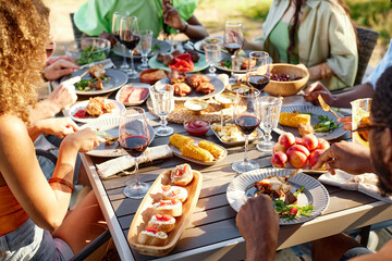 Rustic dinner table outdoors with delicious homemade feast and people enjoying Summer meal...