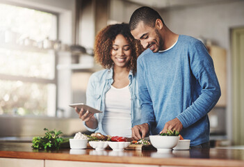 Young, happy and romantic couple cooking healthy food together following recipes online on a...