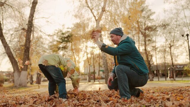 father and little child in an autumn park throw dry leaves up, happy family, live fun with dad, cheerful kid plays with foliage and parent hands throwing leaf fall, parental care of girl, nature walk