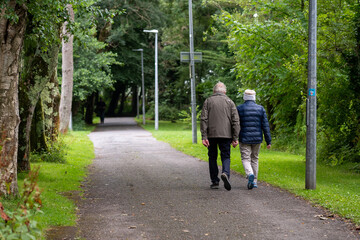 Elderly couple walking in a park side by side holding hands. Love forever theme. Support each other on a way. Stay fit by doing physical activity. Selective focus.