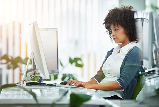 Young female designer working at her computer by a desk in a modern office. Creative business woman in design typing advertising and marketing designs on her pc keyboard at the workplace