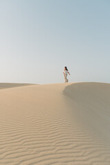 Junge Frau läuft über Sand Dünen vor blauen Himmel vertikal auf Fuerteventura Kanaren