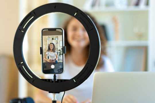 Young curly female blogger recording video at table at home