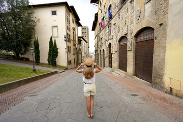 Fototapeta premium Tourism in Italy. Full length of beautiful tourist girl holding hat enjoys visiting the historic town of Arezzo, Tuscany, Italy.