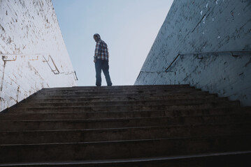 A man stands against the sky at the top of the stone stairs of the underground passage subway back view. Man conquered addiction and gained freedom. Religious and social content. Raise your hands