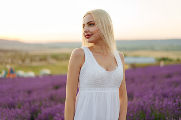 Fototapeta na wymiar Attractive young woman in summer dress standing among the lavender fields
